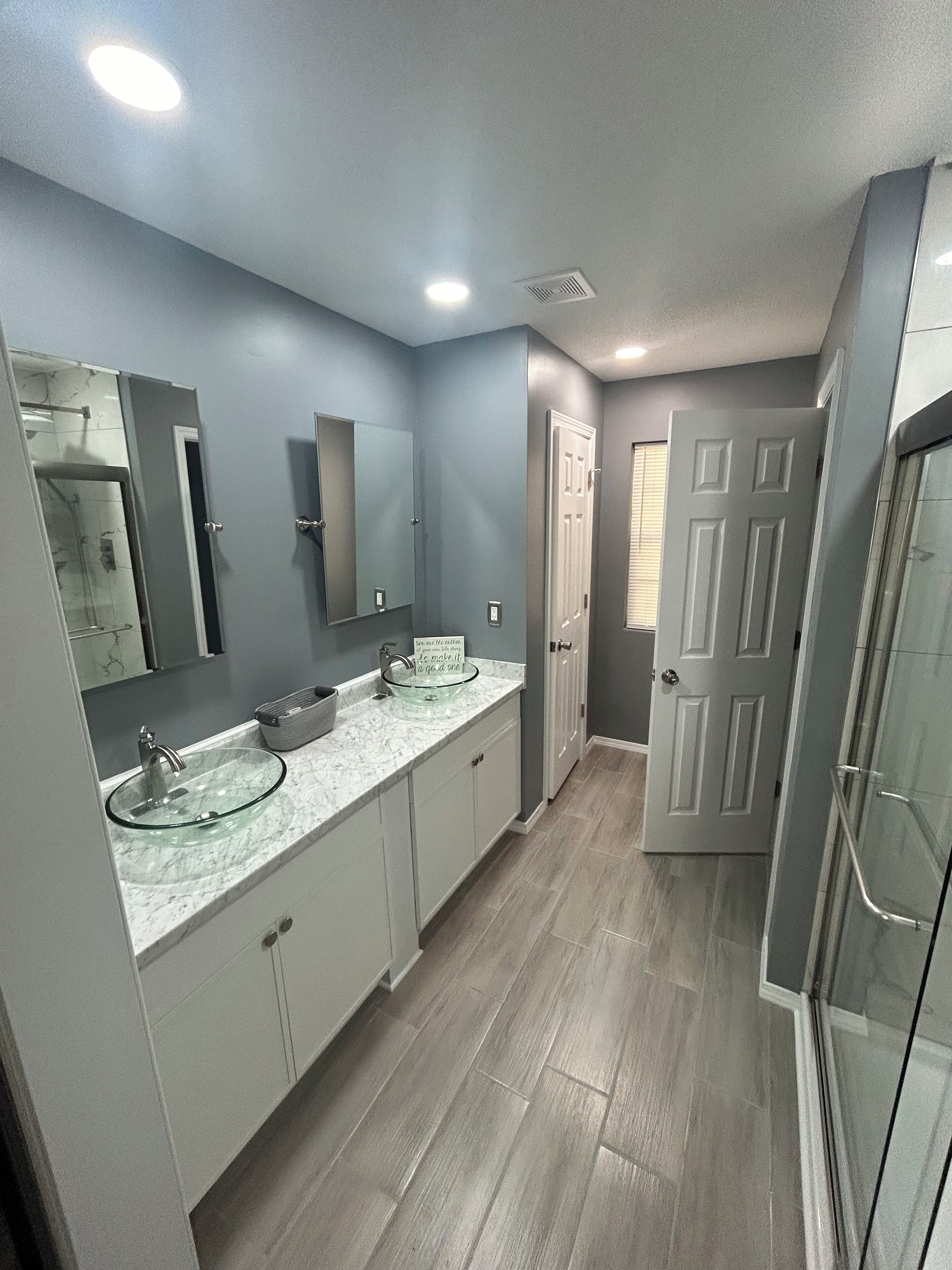 A modern bathroom with a glass-enclosed shower, two sinks with marble countertops, and a large mirror.
