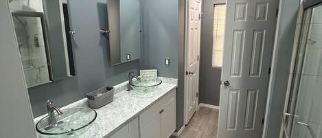 A modern bathroom with a glass-enclosed shower, two sinks with marble countertops, and a large mirror.
