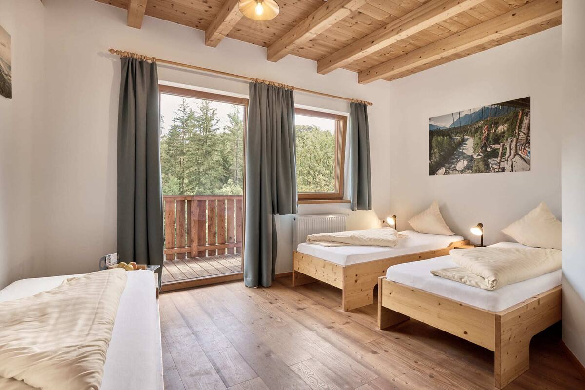 Ein Zimmer mit zwei Holzbetten, einem großen Fenster mit Vorhängen, einer Holzbalkendecke und einem Gemälde an der Wand.