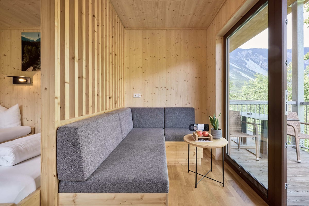 Ein Holzblock-Innenraum mit einer Couch, einem kleinen Tisch und einem Balkon mit Bergblick.