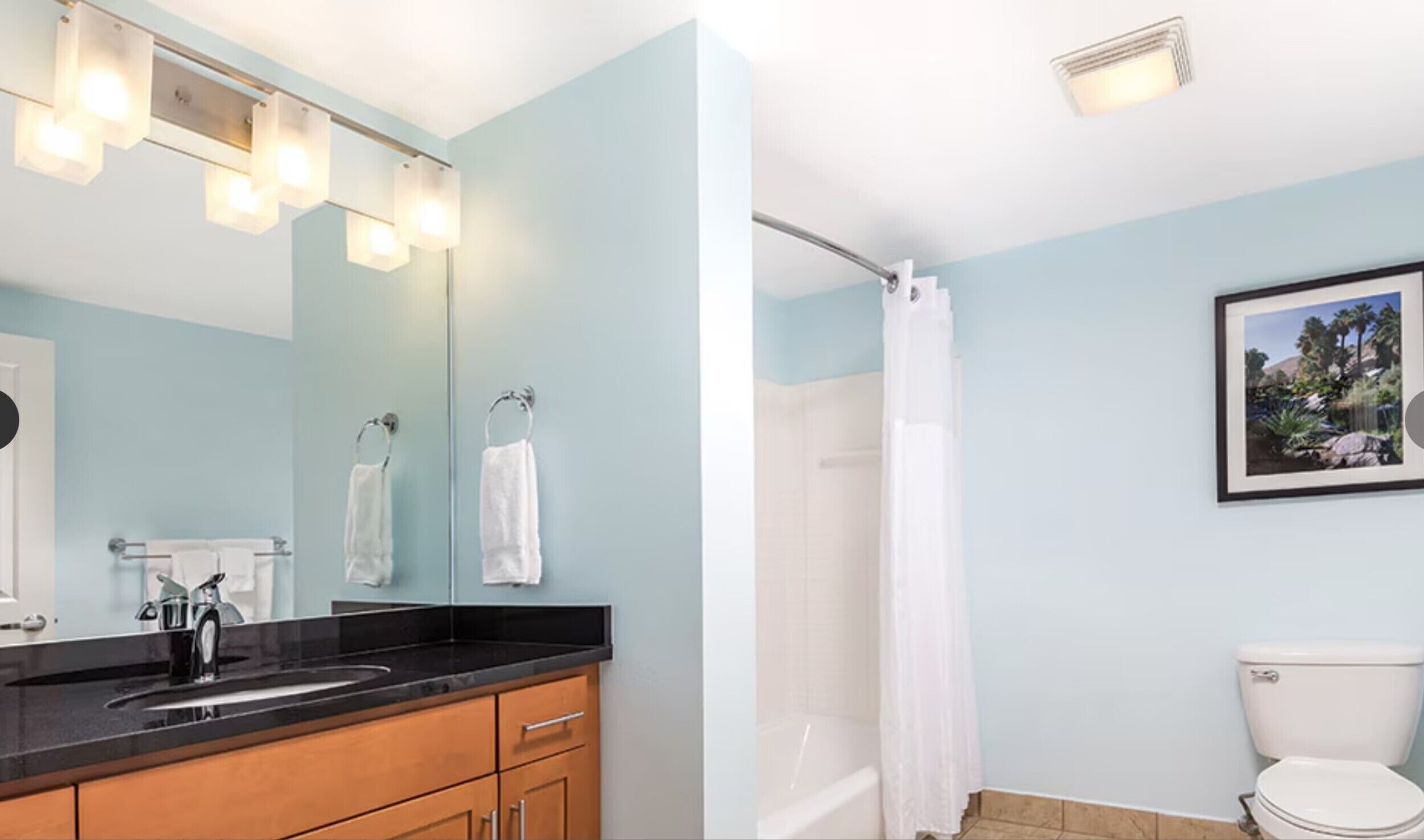 Une salle de bain avec un lavabo à vasque et un plan de toilette noir, un miroir, des toilettes et un rideau de douche.