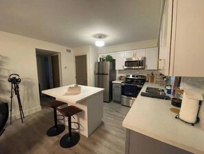 A modern kitchen with white cabinets, stainless steel appliances, and a central island with stools. - Apt in the Heart of Montrose! World Cup Special! (Houston)