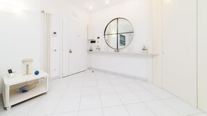 A modern, white bathroom with a round mirror, a small vanity with a lamp, and a shelf with toiletries. - Marescala vacation - Doria Home, spacious apartment in Sorrento town. (Sorrento)