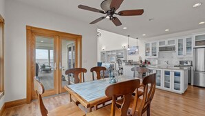 Una cocina moderna con armarios blancos, una isla central y una zona de comedor con sillas de madera y una mesa de mármol.