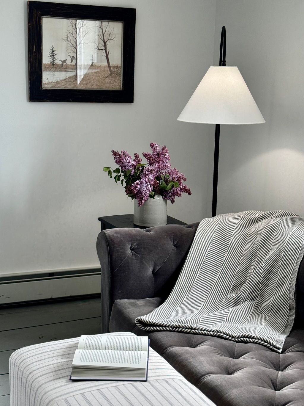A modern living room with a grey sofa, a striped throw pillow, a white lamp, and a framed picture on the wall.