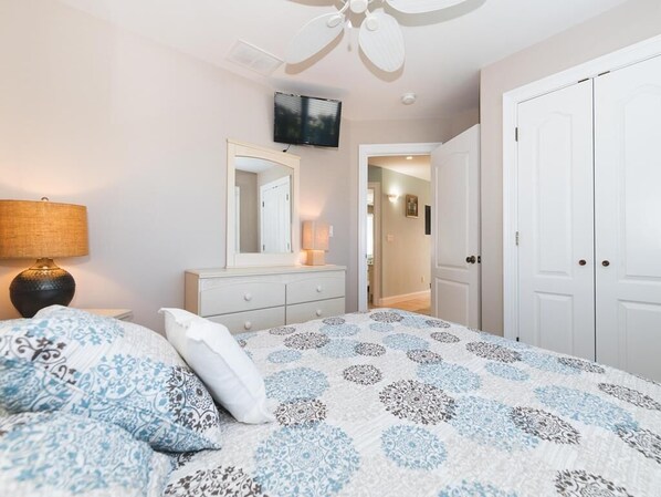 A bedroom with a bed, a dresser, a mirror, a ceiling fan, and a wardrobe.