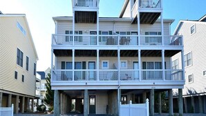 A multi-story building with balconies, a covered entrance, and a gravel driveway. - Spacious 4BR Townhome near the Ocean (North Bethany Beach)
