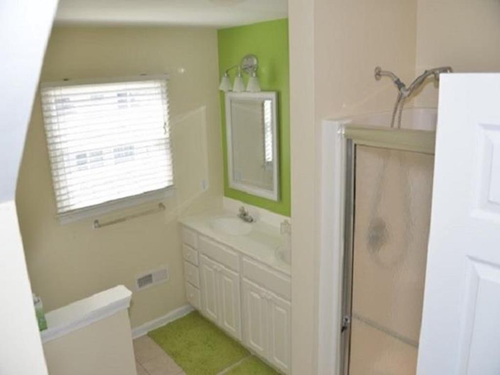 A small bathroom with a window, a mirror, a sink, and a shower.