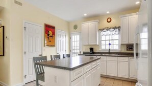 A kitchen with white cabinets, a granite countertop island, and a window with a curtain. - Spacious 4BR Townhome near the Ocean (North Bethany Beach)