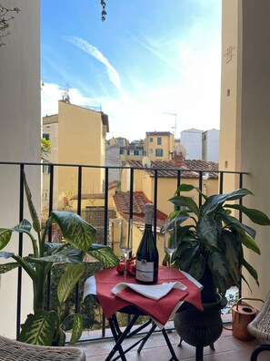 Un balcon avec une table dressée pour deux personnes, une bouteille de vin et des plantes en pot.