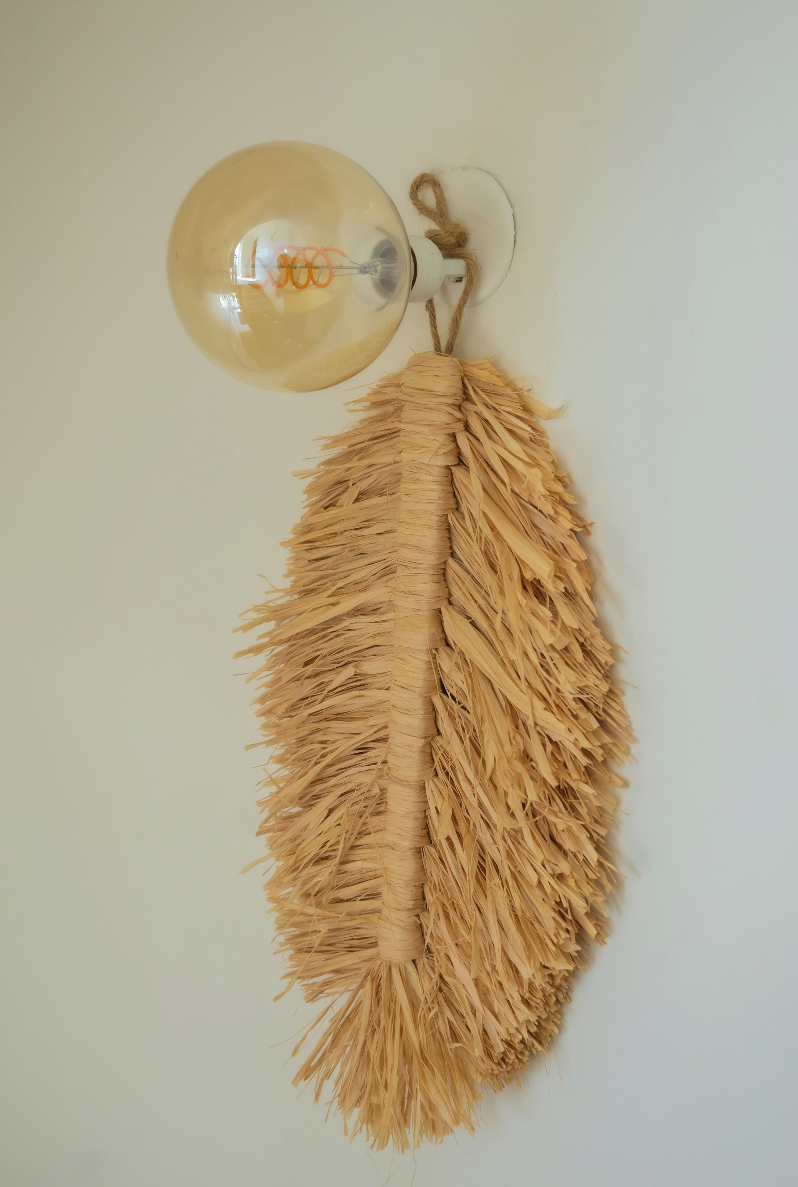 Une lampe murale dotée d’une corde effilochée et d’un tissu texturé, également effiloché, qui pend en dessous.