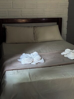 Una cama bien hecha con una colcha marrón y dos toallas blancas dobladas en el centro.