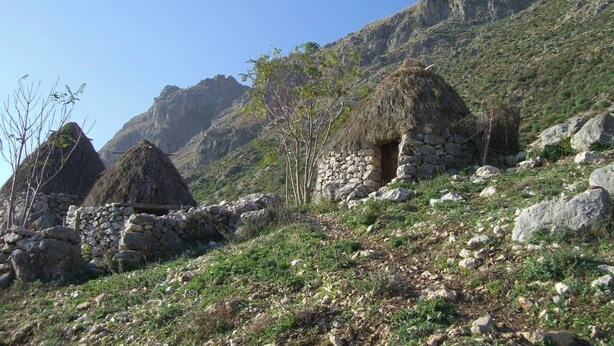 Un paysage montagneux parsemé de cabanes traditionnelles en pierre, sous un ciel bleu azur.