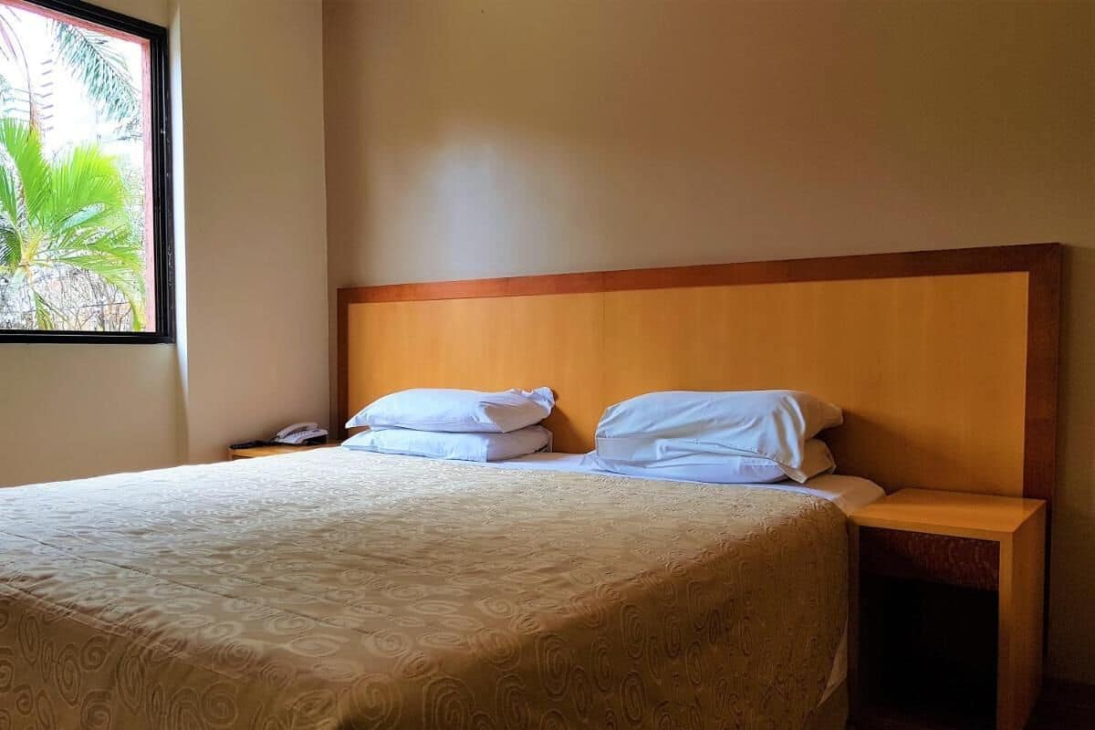 A neatly made bed with a patterned bedspread, a wooden headboard, and a nightstand with a phone.