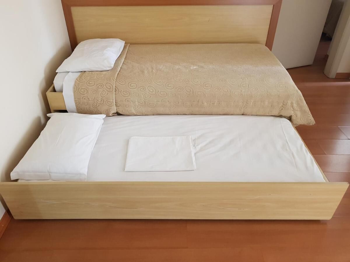 Una cama bien hecha con estructura de madera, colcha beige estampada y sábanas blancas.