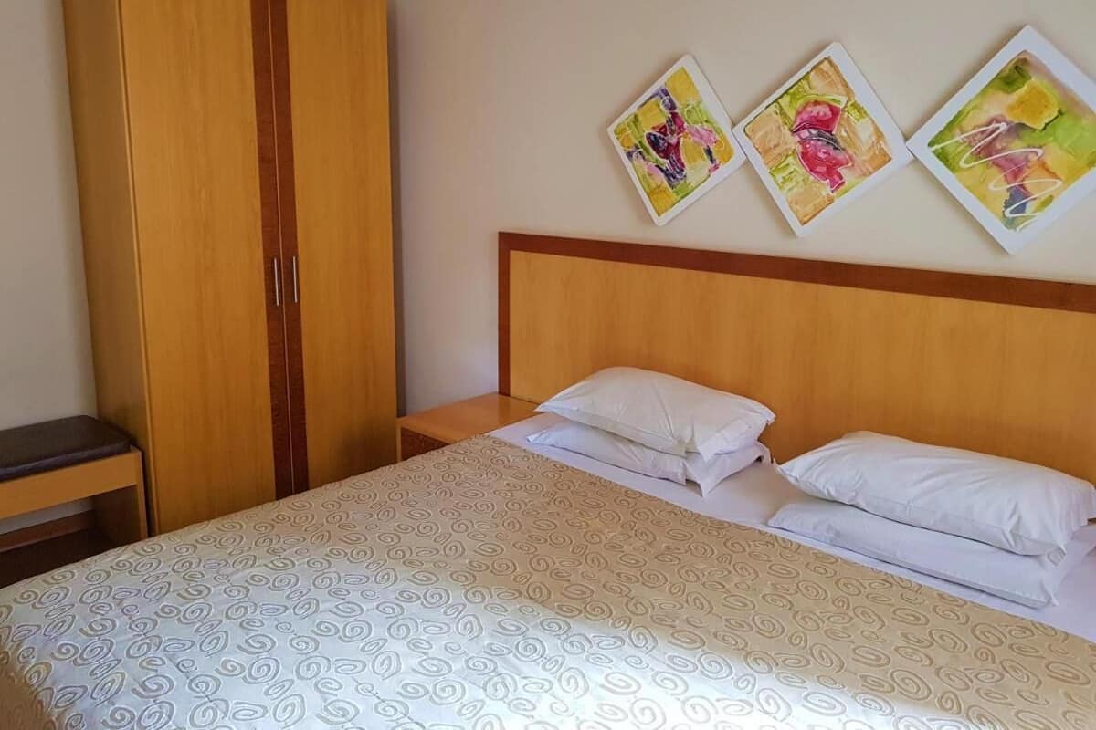 A bedroom with a bed, two pillows, a wooden wardrobe, and three framed pictures on the wall.