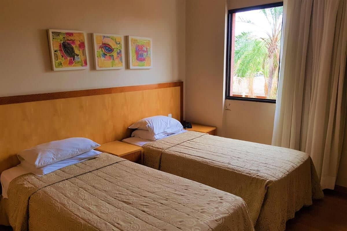 A hotel room with two beds, a wooden headboard, and three colorful paintings on the wall.