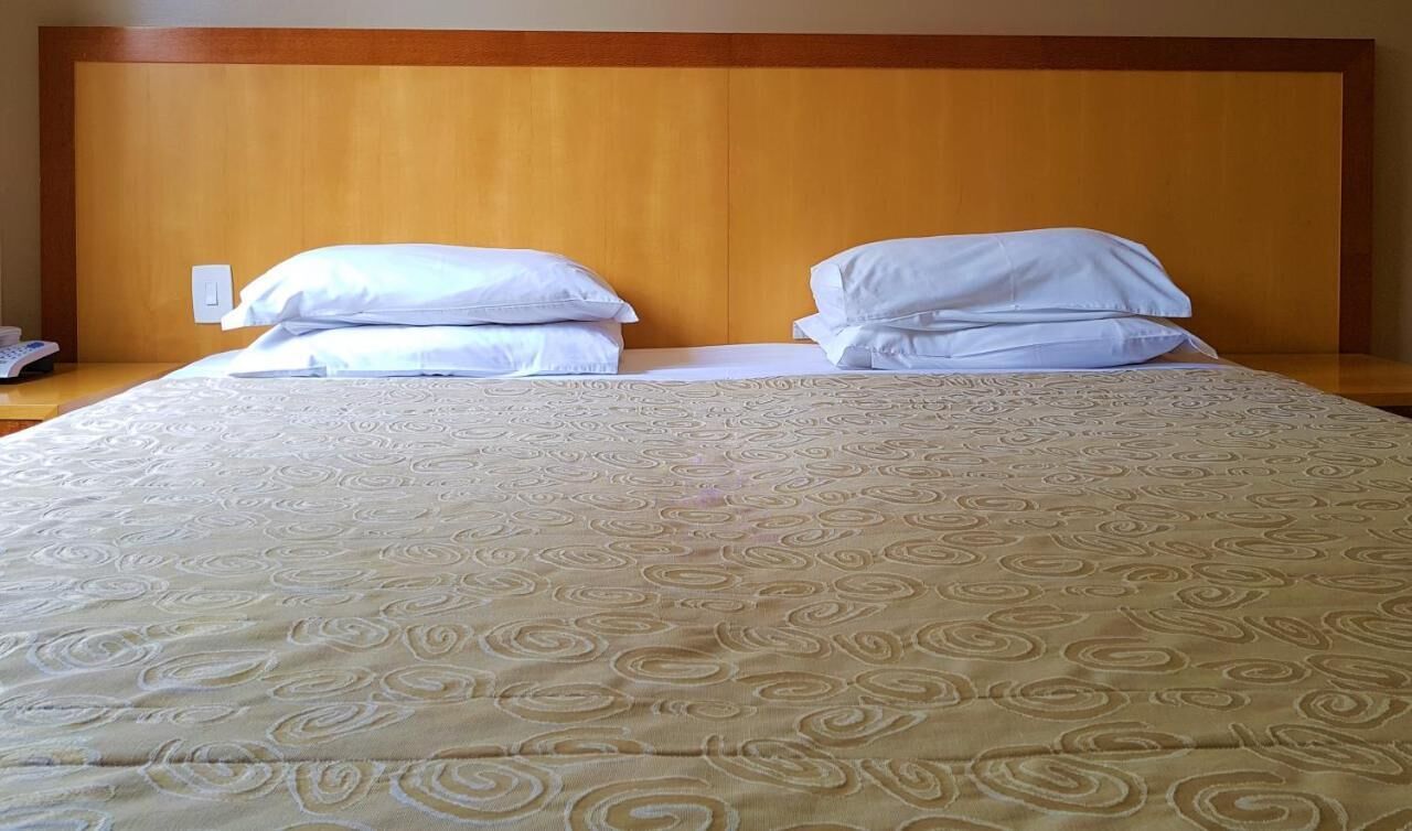 A neatly made bed with a patterned bedspread and two pillows, a wooden headboard, and a bedside table with a phone.