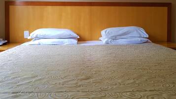 A neatly made bed with a patterned bedspread and two pillows, a wooden headboard, and a bedside table with a phone.