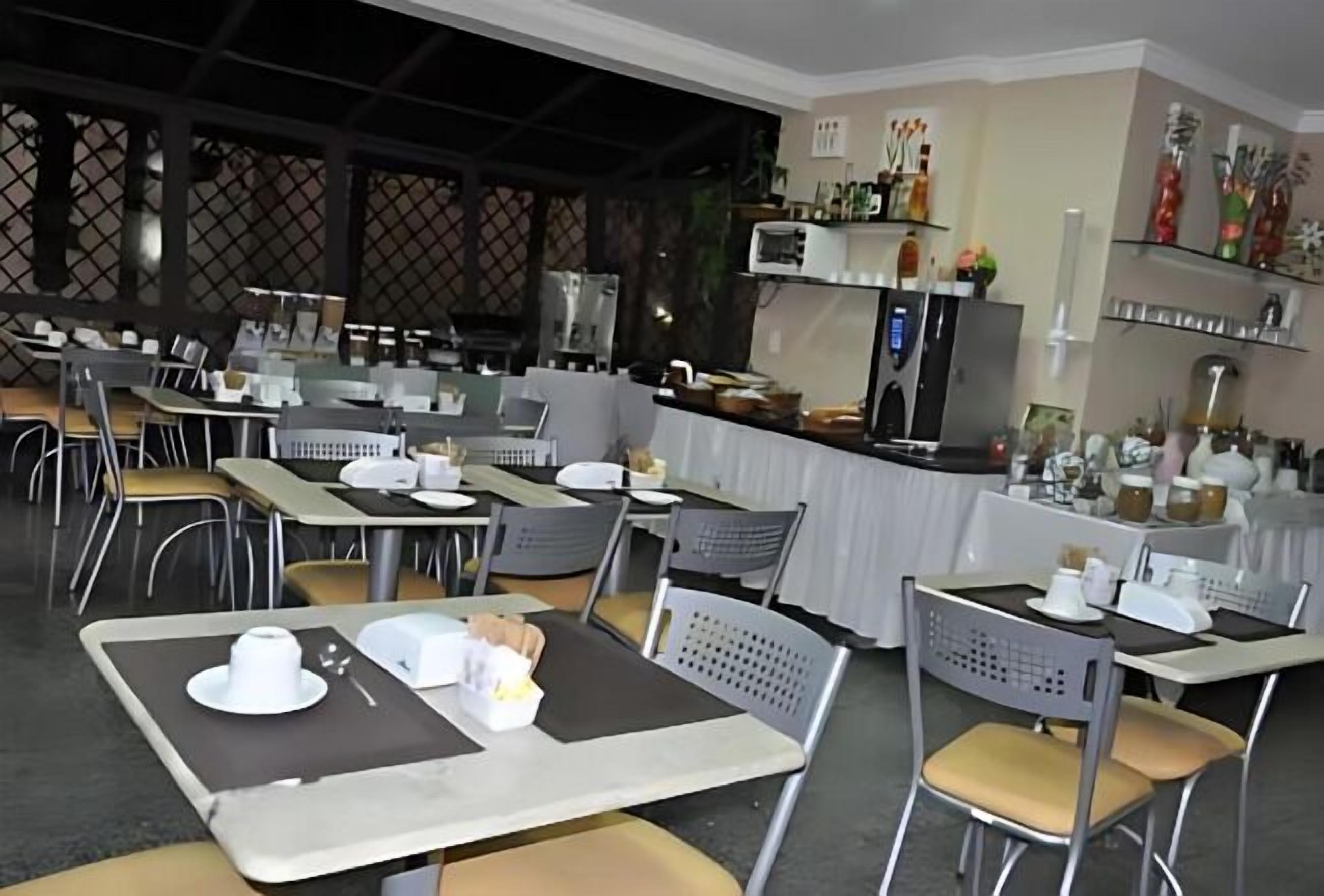 Um restaurante com mesas e cadeiras, um balcão com vitrine e prateleiras com objetos decorativos.