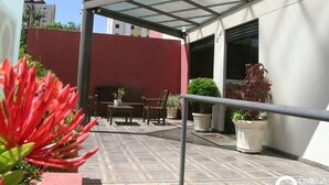 A covered outdoor area with a patio, seating, and potted plants. - Ômega Flat (Bauru)