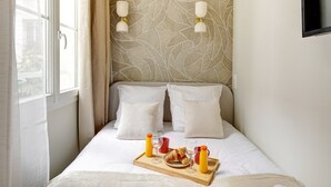 A neatly made bed with white linens, two pillows, a tray with breakfast items, and a patterned wall behind. - TBS 304 - Charming studio in Paris (Paris)