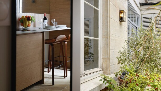 A modern kitchen with wooden cabinets, a dining area with two chairs, and a window overlooking a garden. - TBS 304 - Charming studio in Paris (Paris)