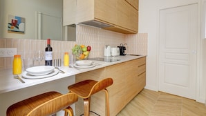 A modern kitchen with wooden cabinets, a white countertop, and two wooden bar stools. - TBS 304 - Charming studio in Paris (Paris)