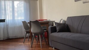 Un salon avec un canapé gris, une table à manger avec des chaises et une fenêtre ornée de rideaux légers.
