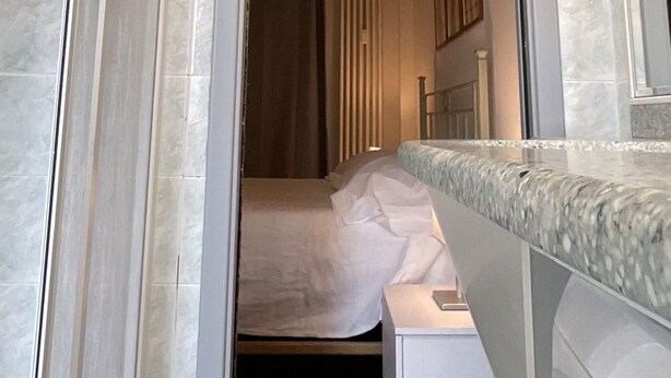 Une salle de bain d’hôtel avec une douche, un miroir et un lit dans la pièce adjacente.
