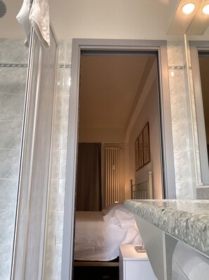 A hotel bathroom with a shower, a mirror, and a bed in the adjacent room. - Valori  (Florence)