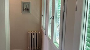 Un couloir étroit avec un radiateur, un tableau encadré au mur et une porte avec une fenêtre.