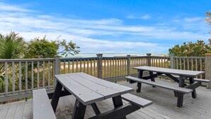 Eine Holzterrasse mit Picknicktischen mit Blick auf einen Strand.