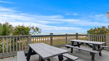A wooden deck with picnic tables overlooking a beach.