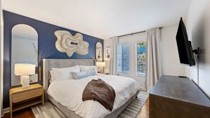Ein modernes Schlafzimmer mit einem großen Bett, Nachttischen, einem Flachbildfernseher und Blick ins Freie.