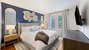 A modern bedroom with a large bed, bedside tables, a flat-screen TV, and a view of the outdoors.
