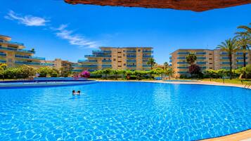 Una gran piscina con dos personas nadando, rodeada de edificios altos y palmeras.