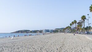 Una extensa playa de arena con algunas personas, cielo despejado y edificios al fondo.