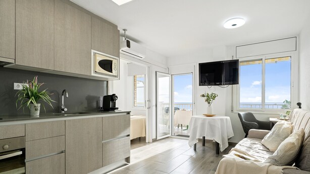 Una cocina moderna con horno empotrado, un comedor con mesa y sillas, y un sofá con vista al mar.