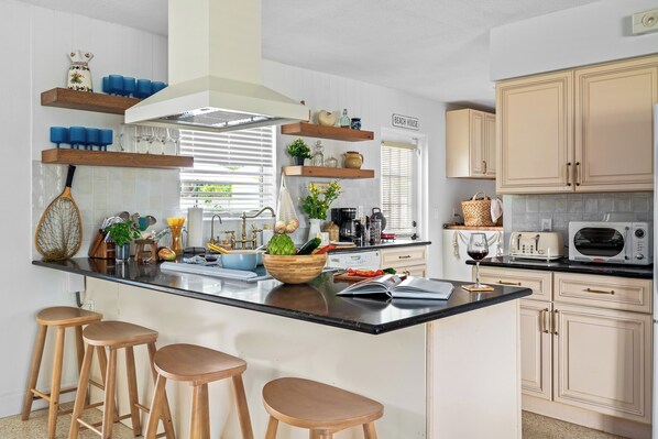 Een moderne keuken met een centraal eiland, barstoelen, houten planken en een bordje met de tekst 