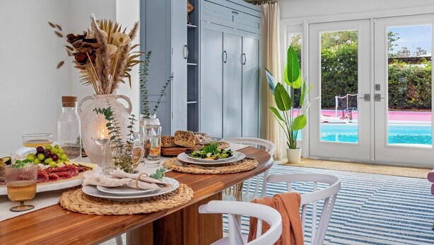 A dining table set with food and drinks, a blue wardrobe, and a view of a swimming pool.