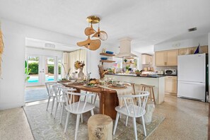 A modern kitchen with white cabinetry, a central island with seating, and a dining area with white chairs. - Heated Pool, Hot Tub & Pickleball Near AMI Beaches (Bradenton)