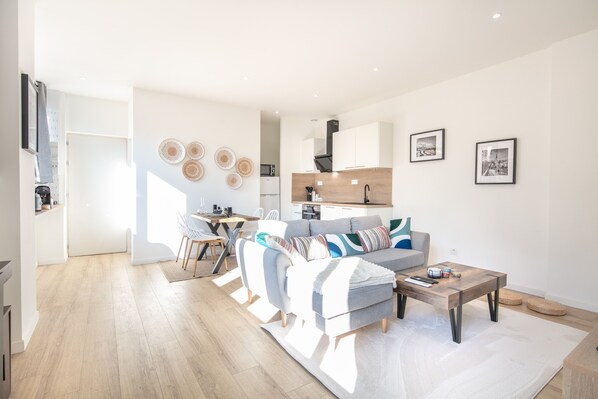 Relax in a spacious living area with a large sofa and coffee table, surrounded by a kitchen with white cabinets and a range hood.