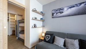Moderni makuuhuone, jossa on kerrossänky, harmaa sohva ja seinälle kiinnitetty hylly, jossa on henkilökohtaisia esineitä.