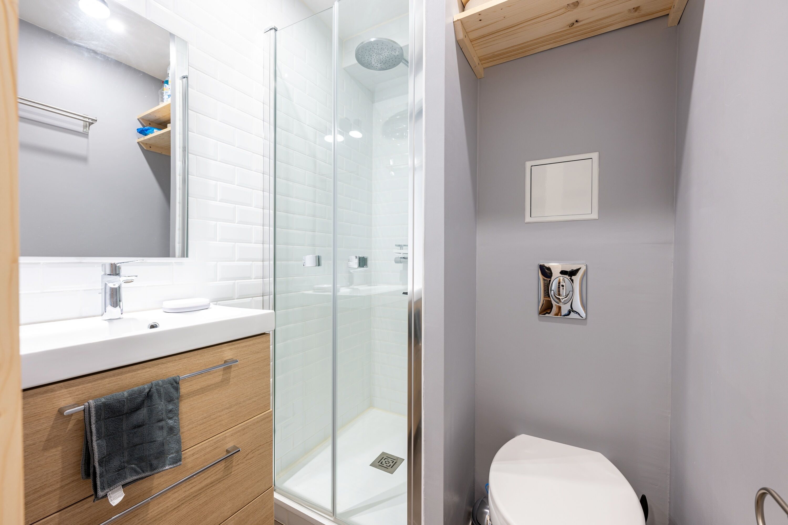 A modern bathroom with a glass-enclosed shower, a white sink, and a wooden vanity.