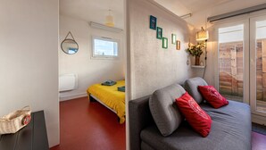 A room with a bed, a sofa, a small table, a window, and a wall-mounted mirror.