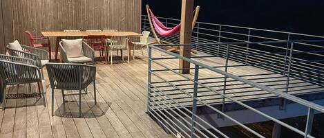 An outdoor deck with wooden flooring, a table with chairs, and a hammock.
