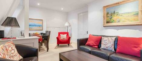 A modern living room with a sofa, armchair, coffee table, and a painting on the wall.