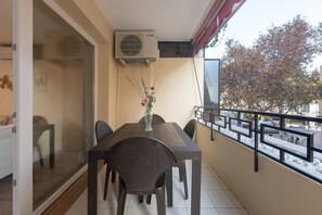 A balcony with a dining table, chairs, and a vase with flowers. An air conditioning unit is mounted on the wall above the table. - Marbella Old Town Apartmet with Parking (Marbella)