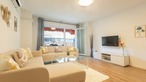 Una sala moderna con sofá, una mesa de centro de vidrio, un televisor de pantalla plana y un mueble bajo de color blanco.